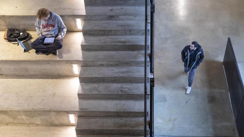 A student walks past the Banvard Gallery and a student sits on the Big Stairs in Knowlton Hall