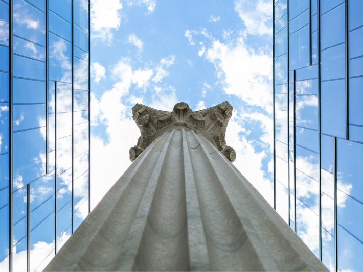 view from below looking up the height of a column into a blue sky with glass reflecting on left and right