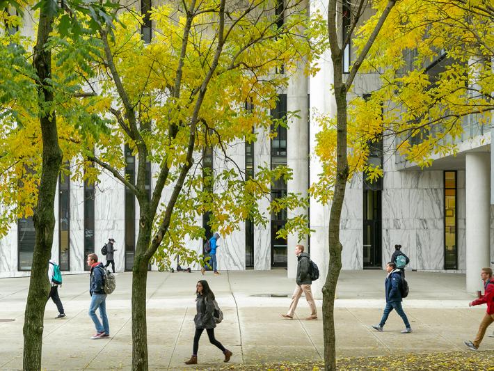 Students walk across Knowlton Hall’s East Patio with autumn leaves in the foreground